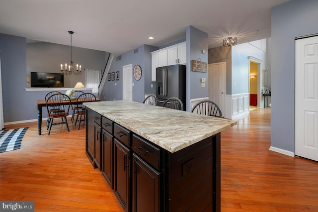 kitchen with decorative light fixtures, black fridge with ice dispenser, light wood-style flooring, and an inviting chandelier