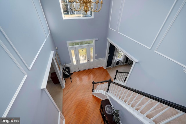 entrance foyer featuring a decorative wall, stairway, a towering ceiling, wood finished floors, and a chandelier