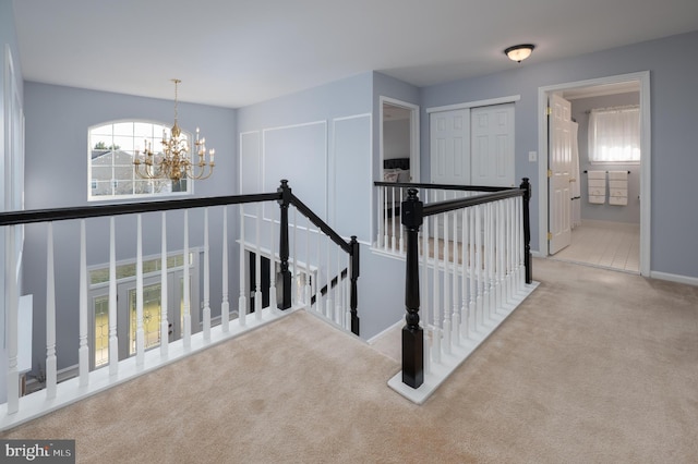 hallway with carpet, baseboards, a notable chandelier, and an upstairs landing