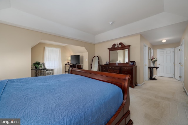 bedroom featuring a raised ceiling, light carpet, and baseboards