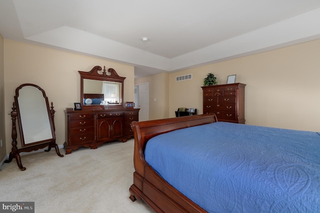 bedroom with a tray ceiling, visible vents, and light carpet