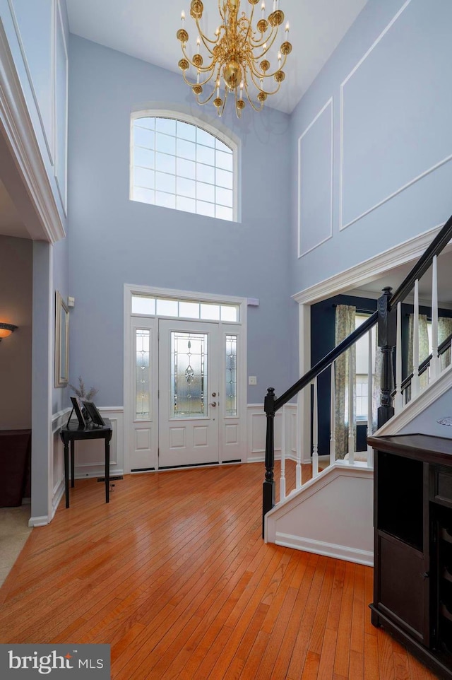 foyer with a wainscoted wall, a notable chandelier, a decorative wall, light wood-style flooring, and stairway