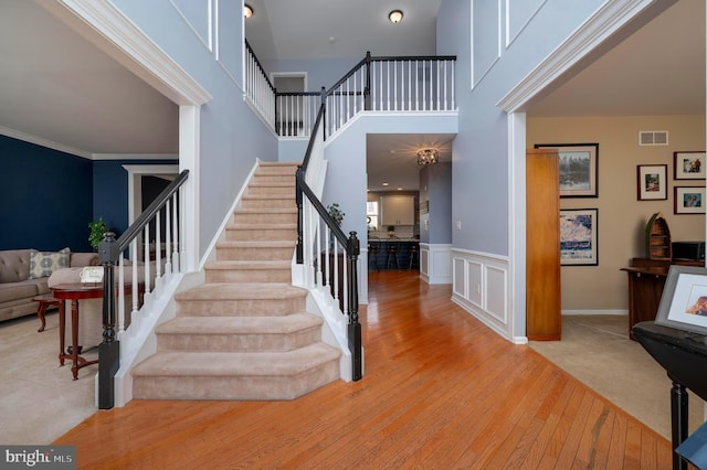 stairway with visible vents, hardwood / wood-style floors, a high ceiling, crown molding, and a decorative wall