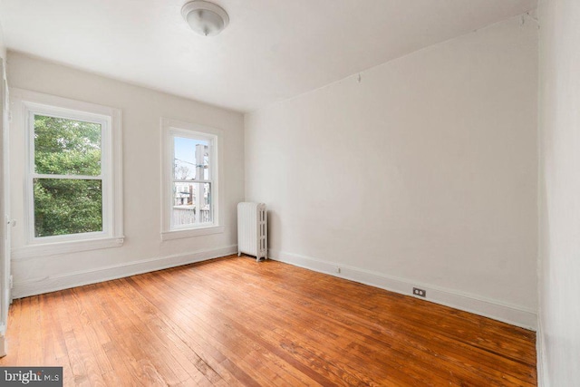 unfurnished room with baseboards, radiator heating unit, and hardwood / wood-style flooring