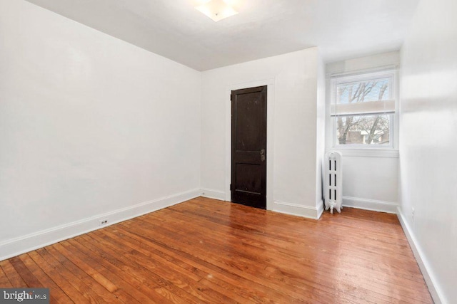 empty room with radiator, baseboards, and hardwood / wood-style flooring