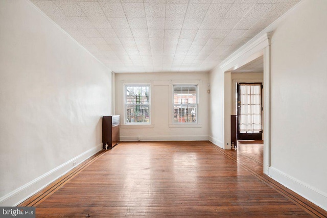 empty room with crown molding, wood finished floors, and baseboards