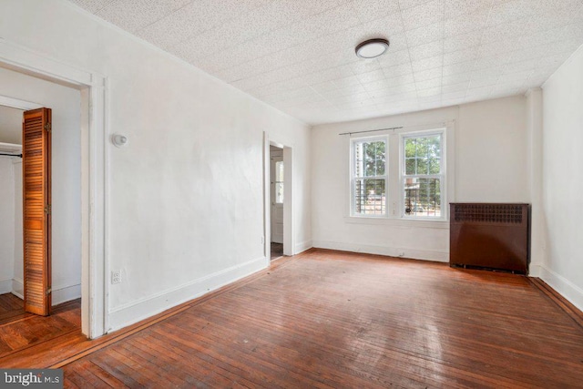 empty room with radiator heating unit, baseboards, and hardwood / wood-style floors