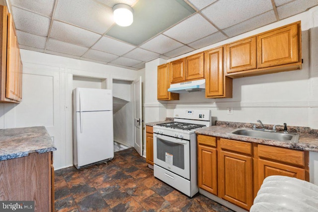 kitchen with white appliances, under cabinet range hood, brown cabinetry, and a sink