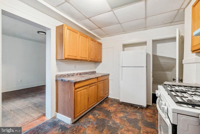 kitchen with a paneled ceiling, white appliances, baseboards, light countertops, and stone finish flooring