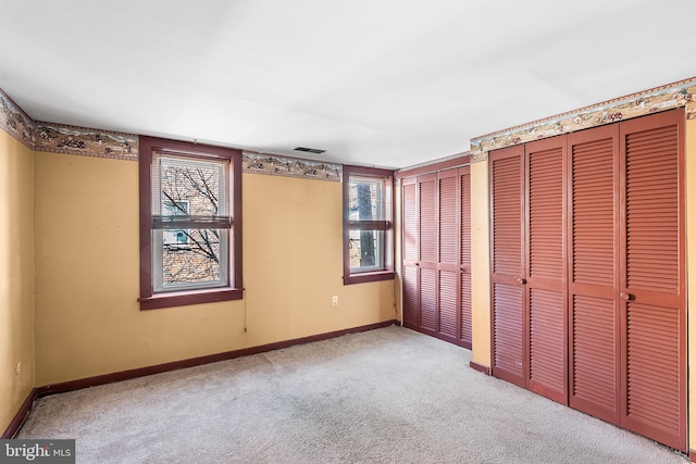 unfurnished bedroom with carpet, visible vents, baseboards, and two closets