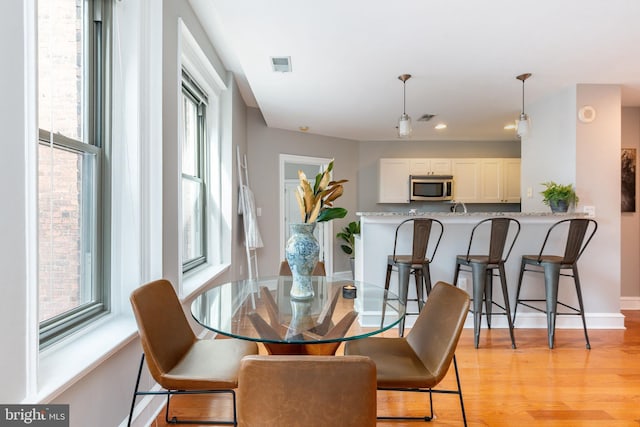 dining area with light wood-type flooring, visible vents, and baseboards