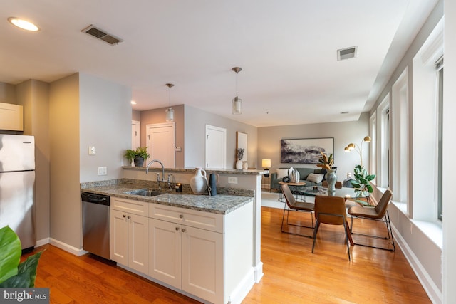 kitchen with stainless steel appliances, a peninsula, a sink, visible vents, and light wood finished floors