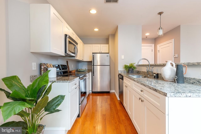 kitchen with a peninsula, a sink, white cabinets, light wood-style floors, and appliances with stainless steel finishes