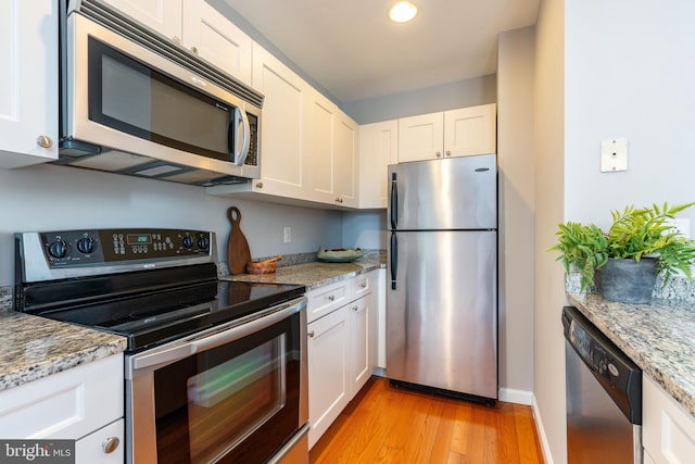 kitchen with light stone counters, stainless steel appliances, light wood-style flooring, white cabinetry, and baseboards