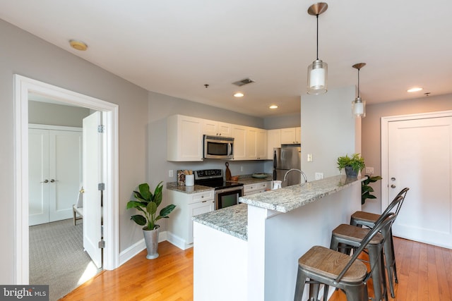 kitchen featuring stainless steel appliances, a peninsula, visible vents, light wood finished floors, and a kitchen bar