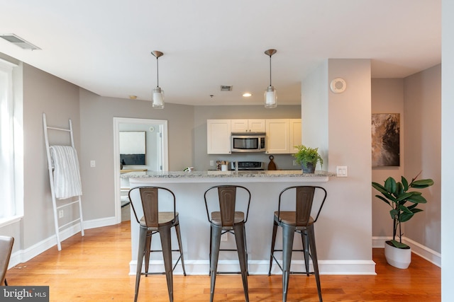 kitchen featuring stove, visible vents, a kitchen breakfast bar, light wood-style floors, and stainless steel microwave