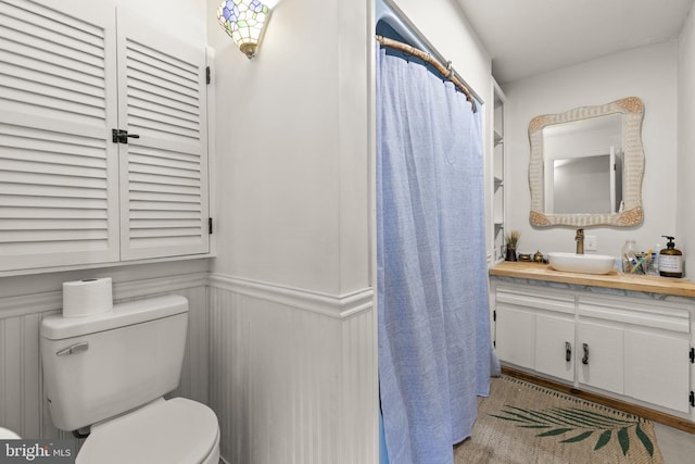 full bathroom with a wainscoted wall, a decorative wall, toilet, vanity, and a shower with curtain