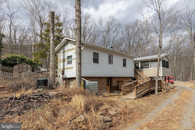 rear view of property with central AC unit, a sunroom, stairway, fence, and brick siding