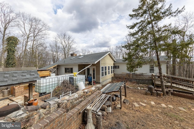 rear view of house featuring a shingled roof, a chimney, and an outdoor structure