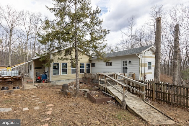 back of house featuring a shingled roof, fence, and a garden