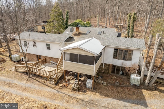 rear view of property with a chimney, a shingled roof, stairway, a sunroom, and a wooden deck