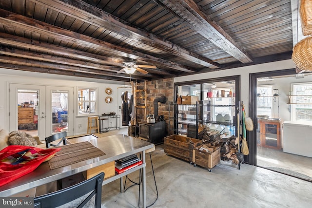 dining space with a ceiling fan, french doors, beam ceiling, unfinished concrete flooring, and a wood stove