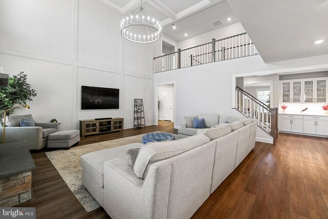 living room with dark wood-style flooring, beam ceiling, a towering ceiling, a chandelier, and stairs