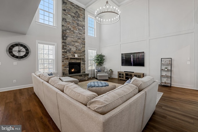 living area featuring a chandelier, a stone fireplace, dark wood-style flooring, and baseboards