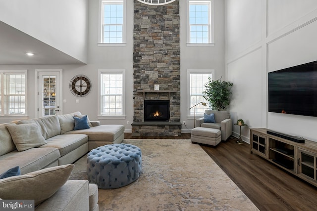 living area featuring dark wood-style floors, baseboards, a fireplace, and a high ceiling