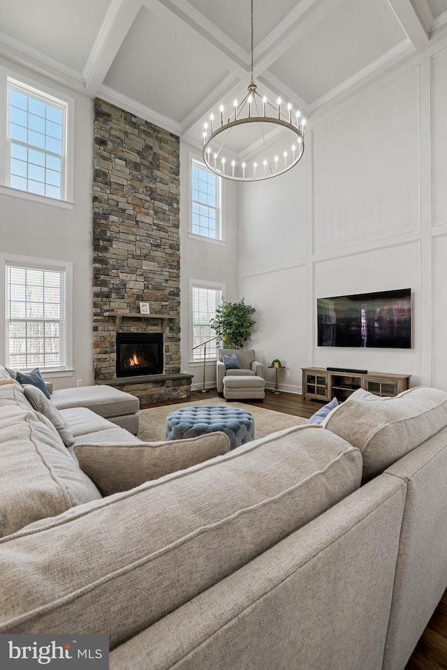 living area featuring a stone fireplace, coffered ceiling, wood finished floors, a towering ceiling, and ornamental molding