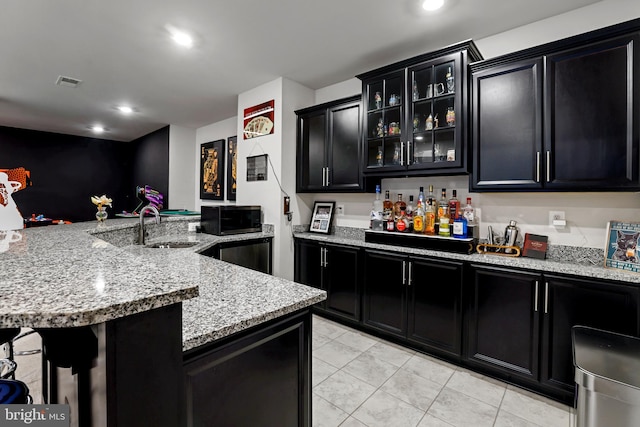 kitchen featuring a breakfast bar, visible vents, dark cabinetry, light stone countertops, and glass insert cabinets