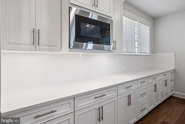 kitchen featuring dark wood finished floors, tasteful backsplash, light countertops, white cabinetry, and built in microwave