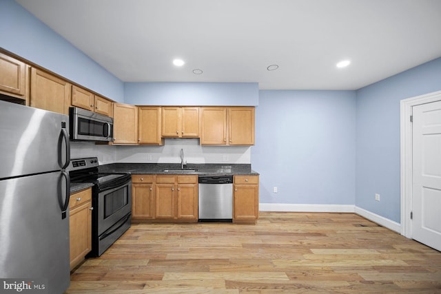 kitchen with stainless steel appliances, baseboards, a sink, and light wood finished floors