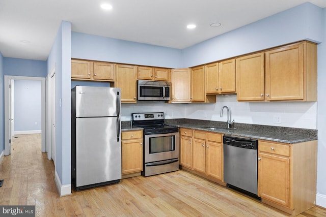 kitchen with appliances with stainless steel finishes, light wood-type flooring, a sink, and baseboards