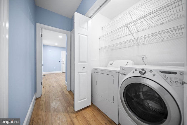 laundry area with laundry area, baseboards, light wood finished floors, and washing machine and clothes dryer