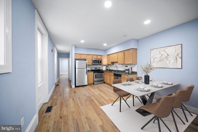 kitchen featuring light wood finished floors, stainless steel appliances, dark countertops, visible vents, and baseboards