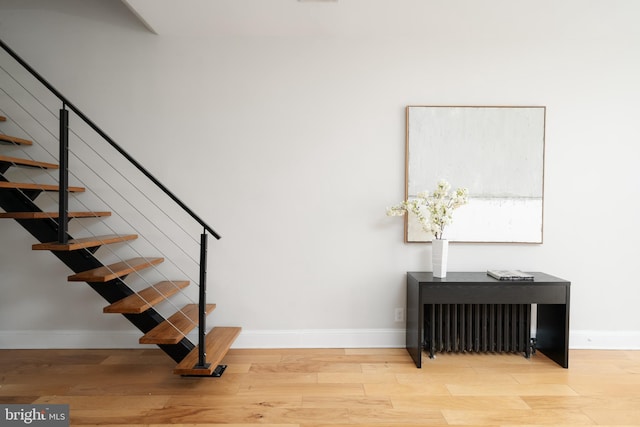 staircase with baseboards, wood finished floors, and radiator