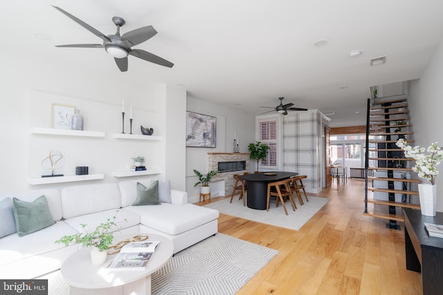 living room with visible vents, a ceiling fan, a glass covered fireplace, light wood-style flooring, and stairway