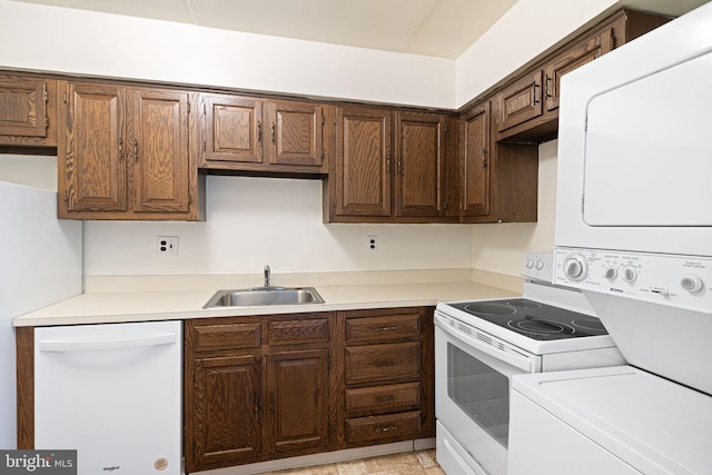 kitchen featuring white appliances, stacked washing maching and dryer, a sink, light countertops, and dark brown cabinetry