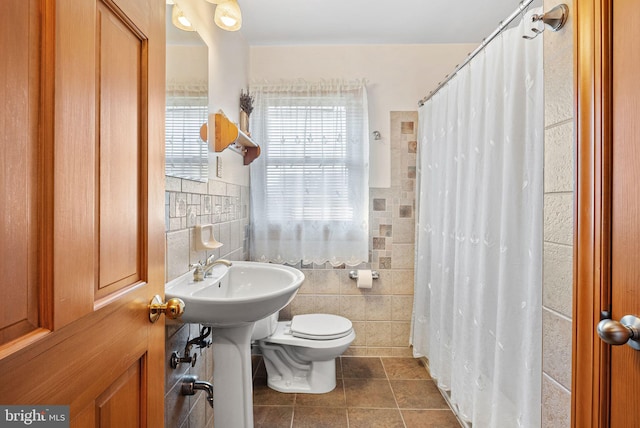 bathroom with toilet, curtained shower, tile patterned flooring, and tile walls