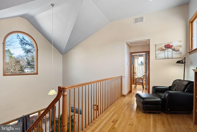 corridor with light wood-type flooring, visible vents, vaulted ceiling, and an upstairs landing