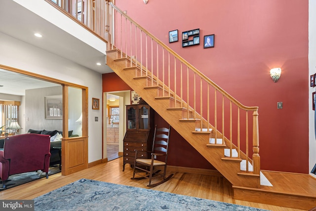 stairs featuring recessed lighting, baseboards, a high ceiling, and wood finished floors