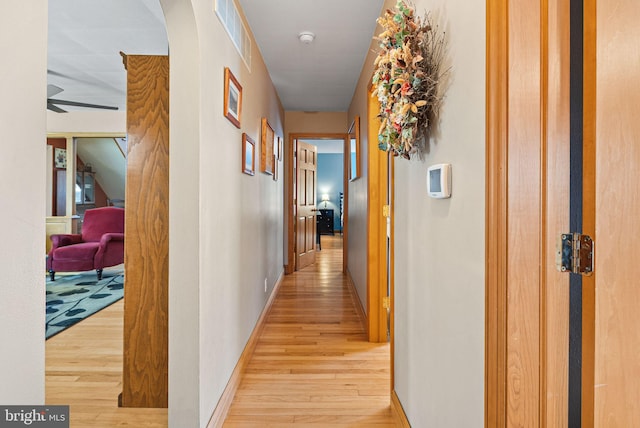 corridor with light wood finished floors, visible vents, and baseboards