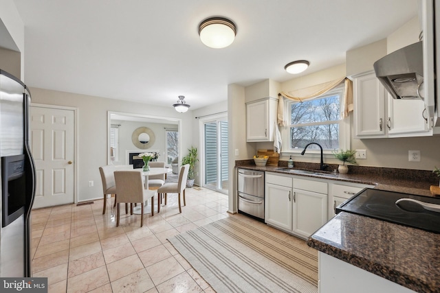 kitchen with light tile patterned floors, white cabinets, wall chimney exhaust hood, stainless steel appliances, and a sink