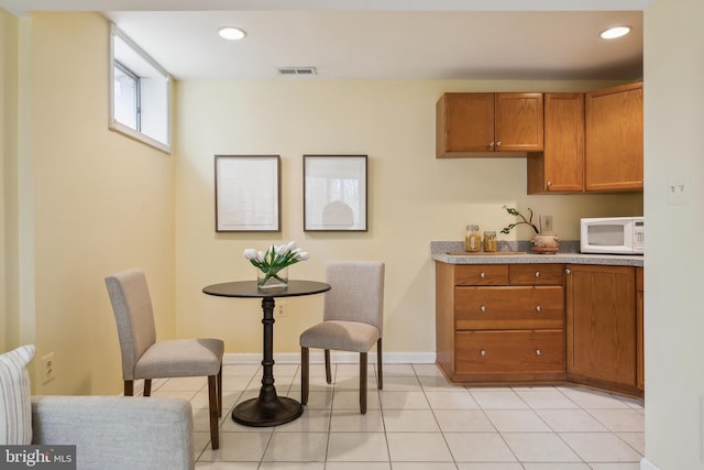 kitchen featuring light tile patterned floors, visible vents, brown cabinetry, white microwave, and recessed lighting