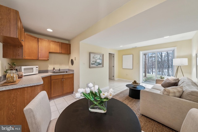 kitchen with light tile patterned floors, light countertops, white microwave, open floor plan, and a sink