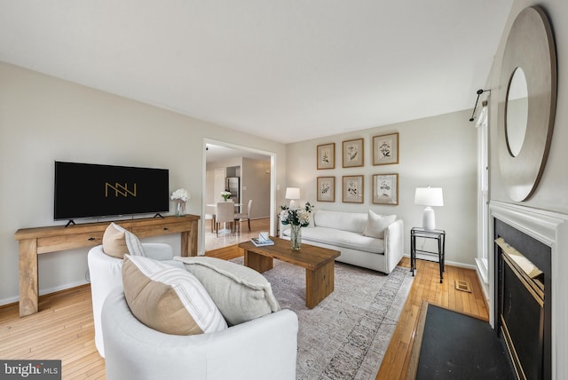 living area with a fireplace, light wood-style flooring, and baseboards