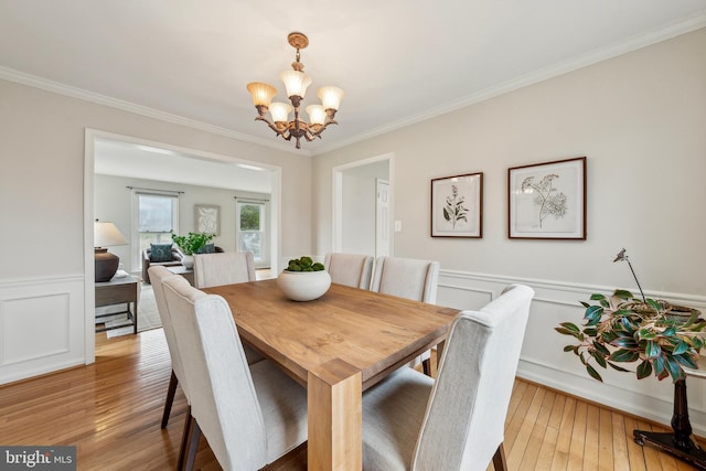 dining space with a wainscoted wall, an inviting chandelier, crown molding, light wood-type flooring, and a decorative wall