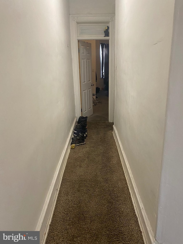 corridor featuring baseboards and dark carpet