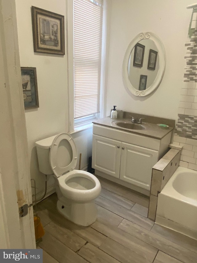 bathroom with a washtub, wood finish floors, vanity, and toilet